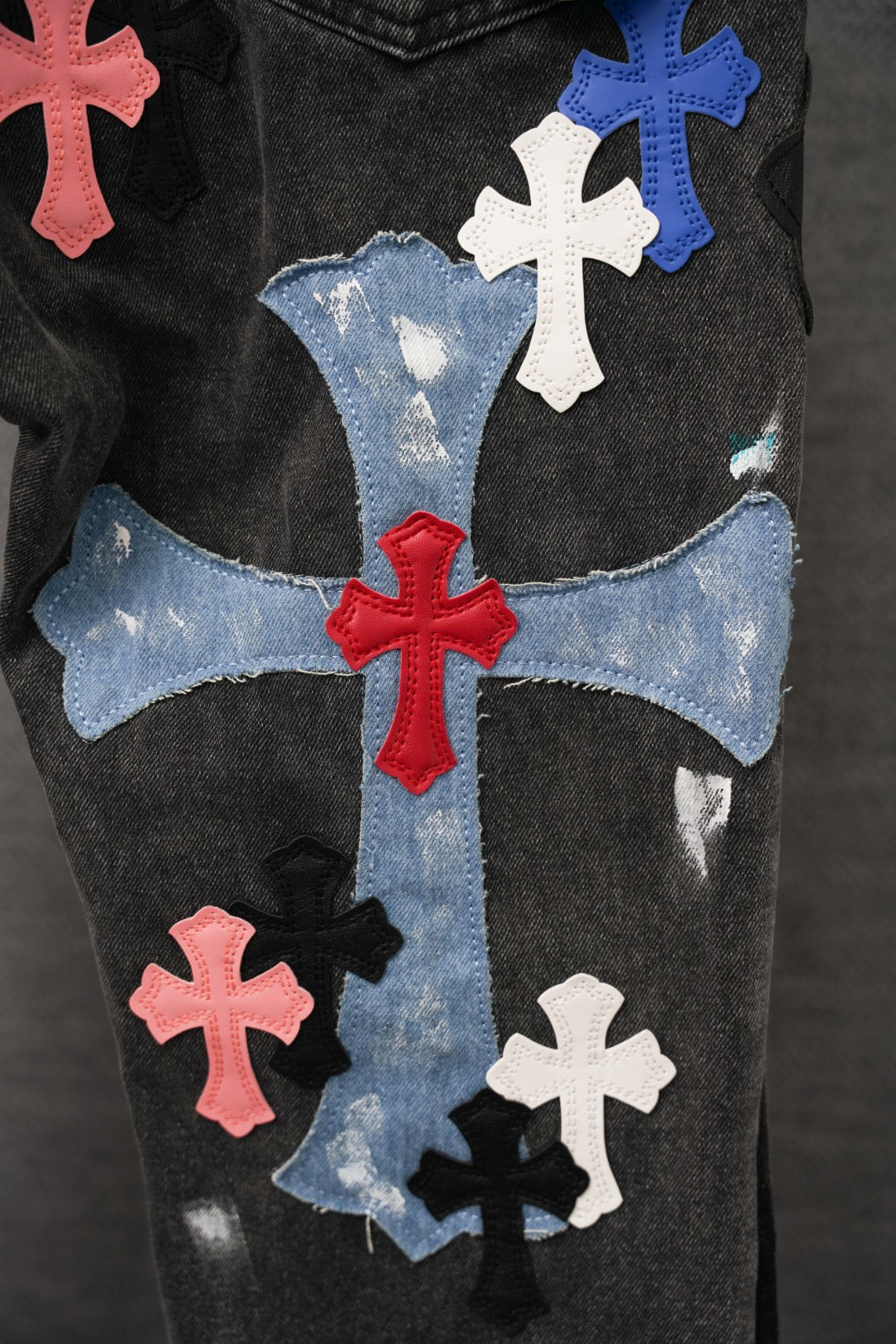 Black denim pants close-up: large cross graphic patchwork on front leg