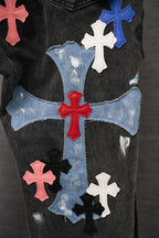 Dark denim pants with large blue cross patch design across the front