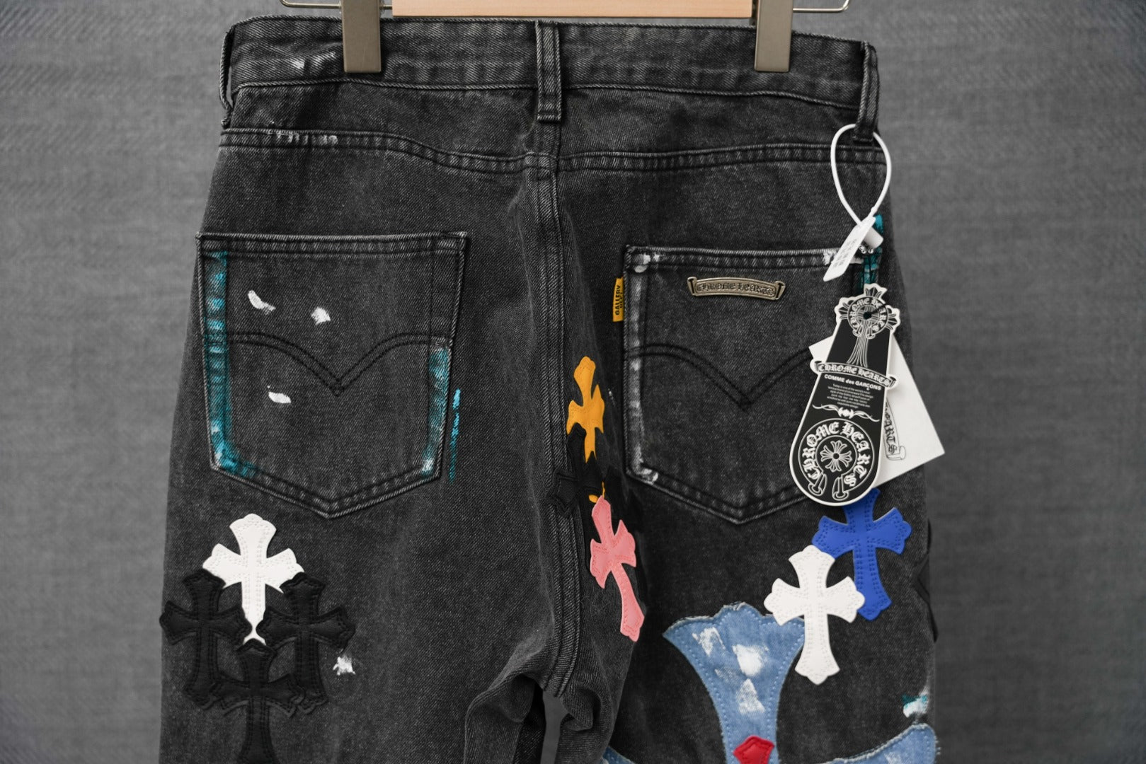 Black denim pants with colorful cross patches on front, belt loops and pockets