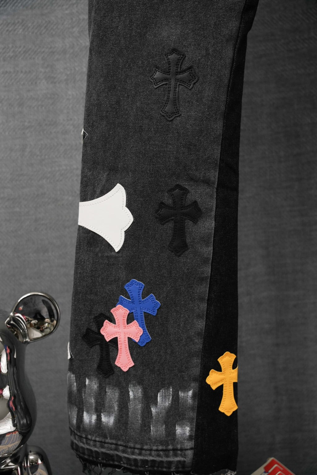 Black denim pants with scattered cross patches on the leg and hem