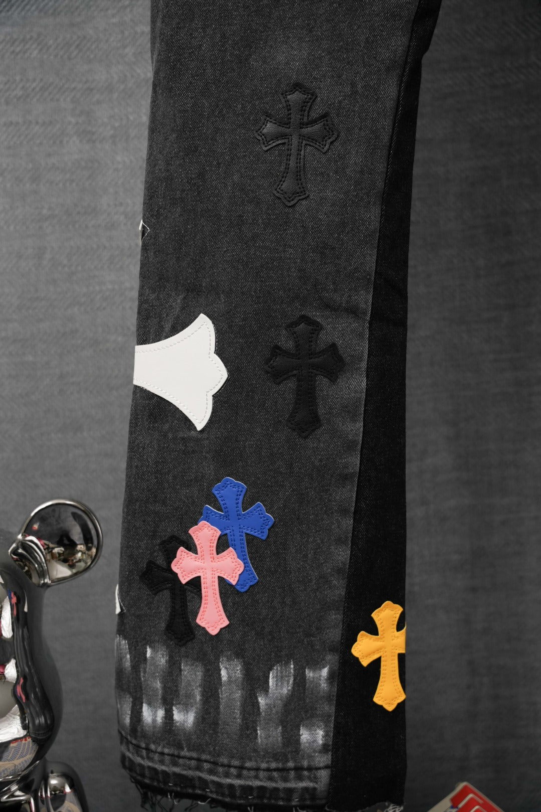 Black denim pants with scattered cross patches on the leg and hem