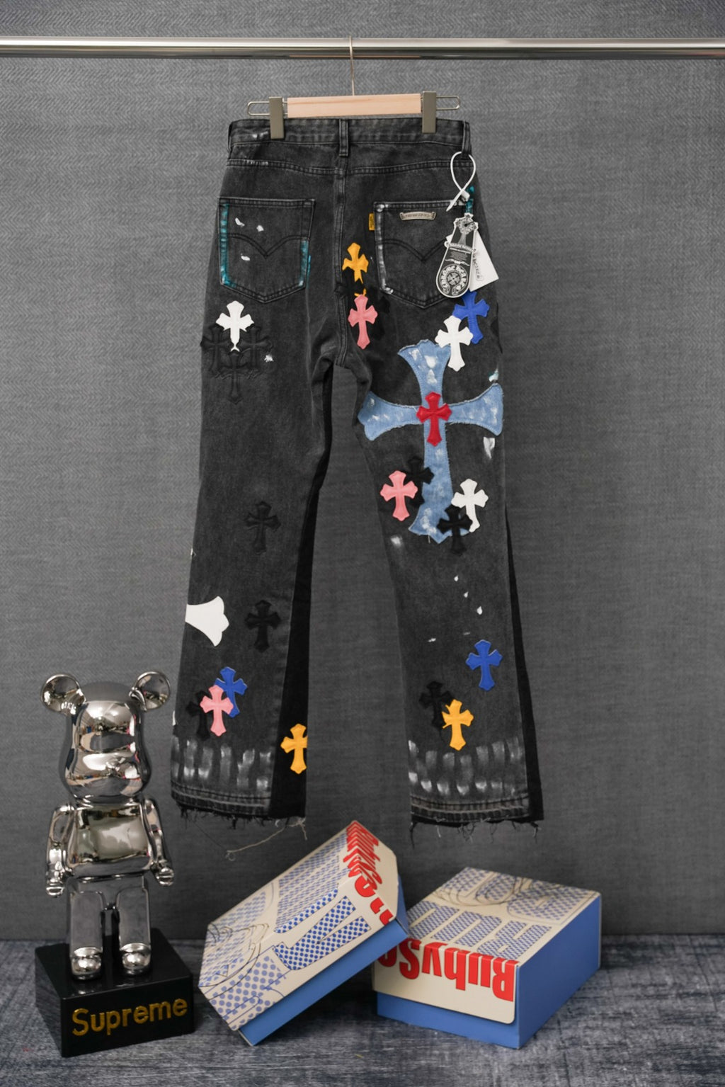 Black denim pants with multicolor cross appliques and distressed wash, hanging view