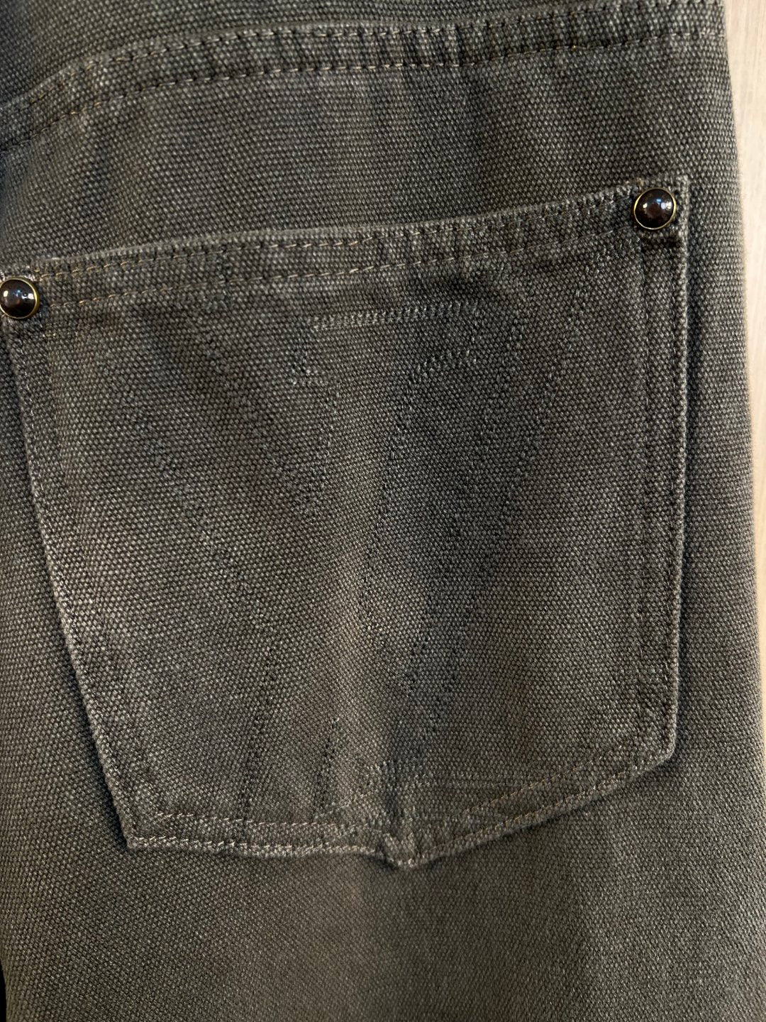 Front pocket close-up with metal button and visible stitching on dark gray denim
