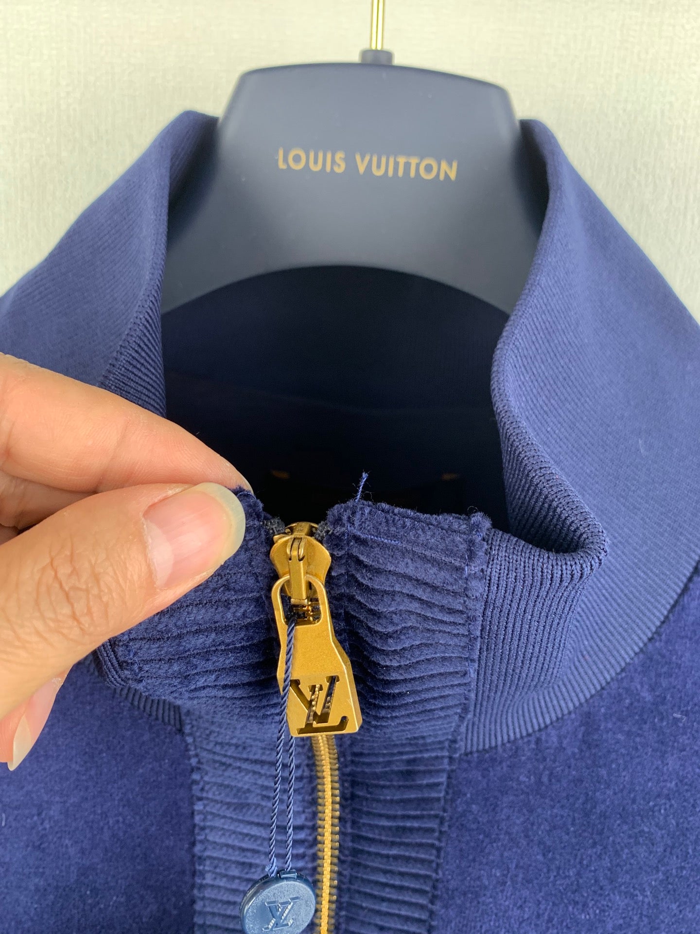 Blue Louis Vuitton jacket zipper pull detail with gold LV charm and ribbed collar