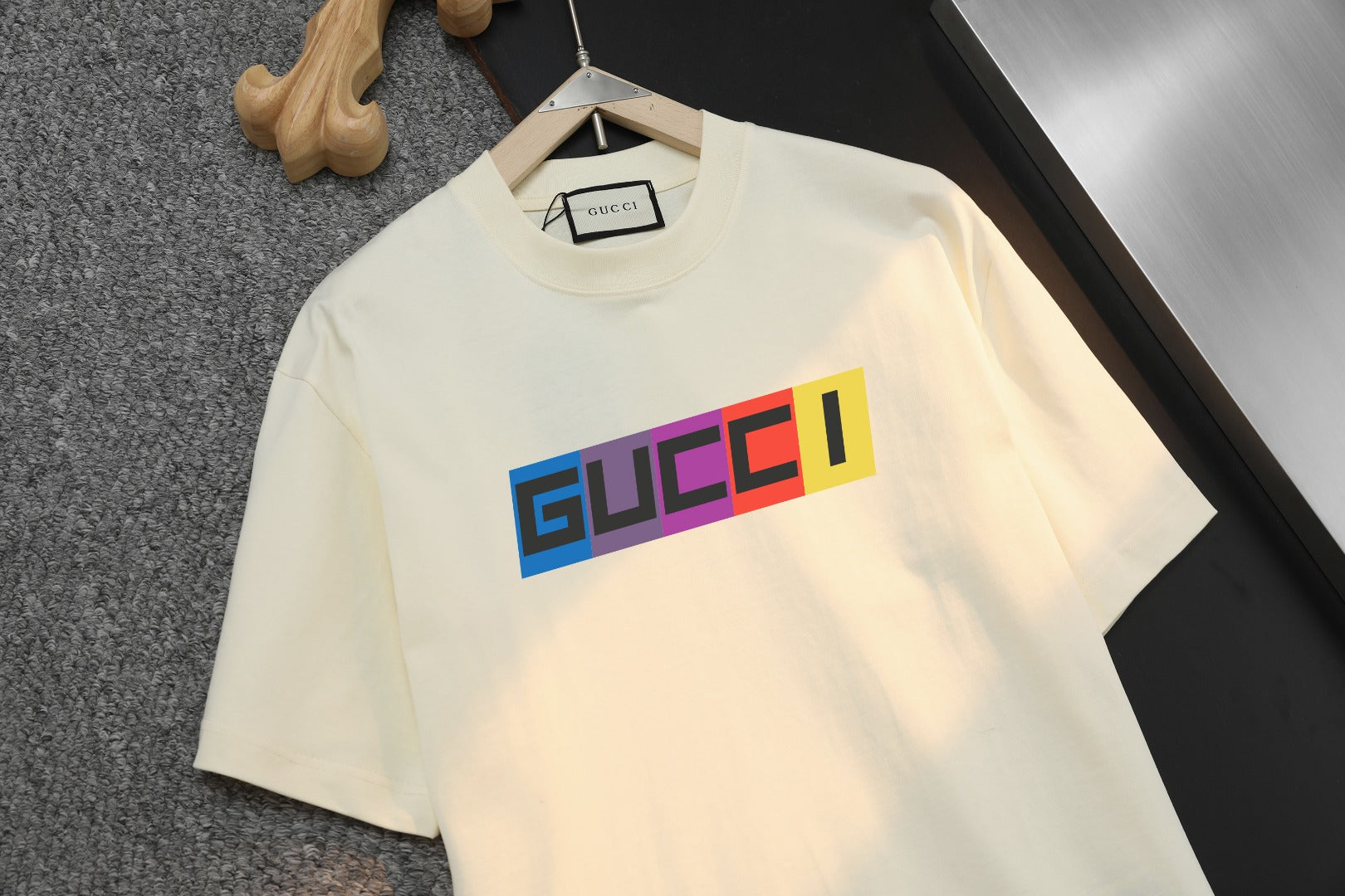Cream Gucci T-shirt close-up, bold multicolor logo across chest, crew neck.