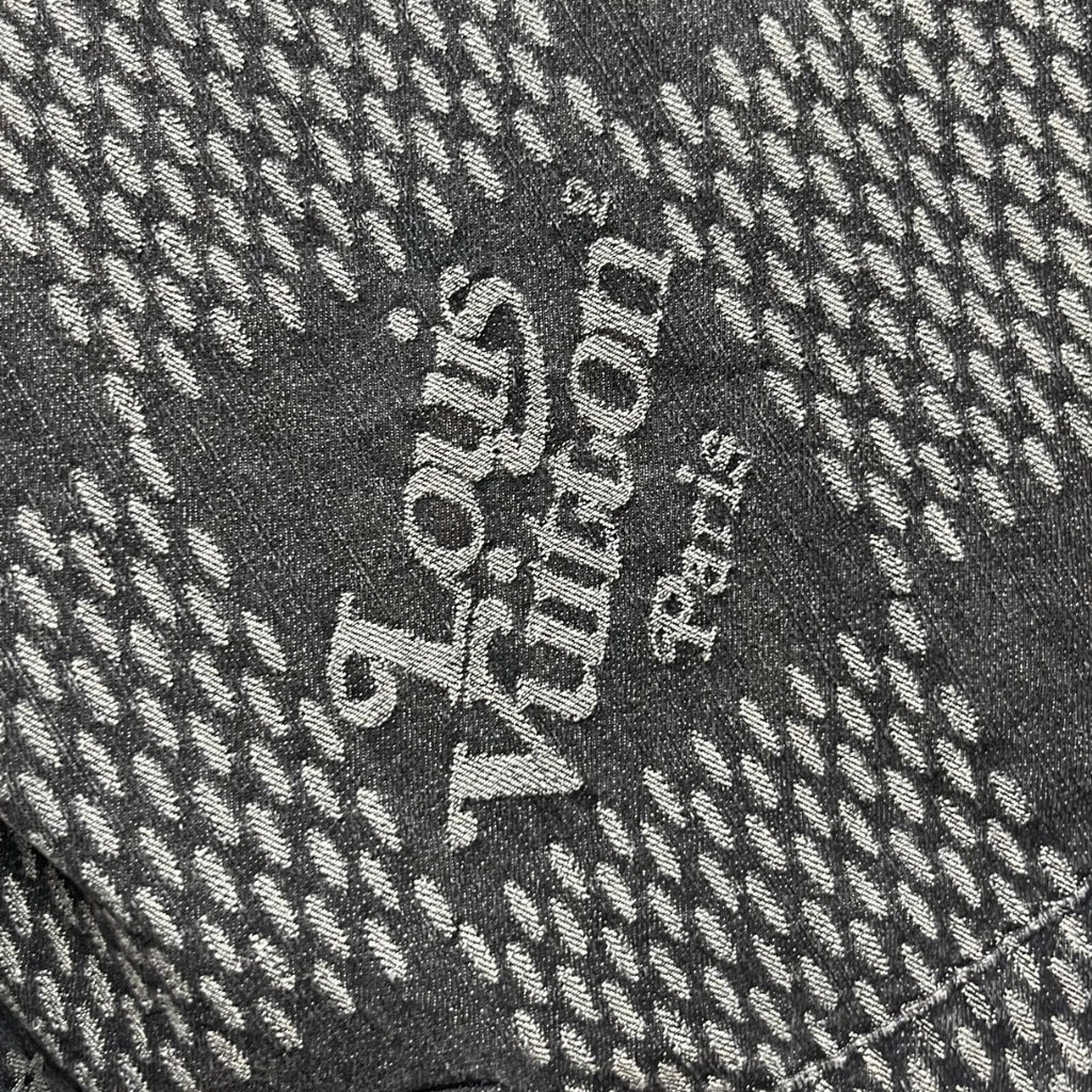 Louis Vuitton denim fabric detail with large white text on dark herringbone pattern