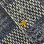 Denim fabric close-up with monogram pattern and small gold logo snap