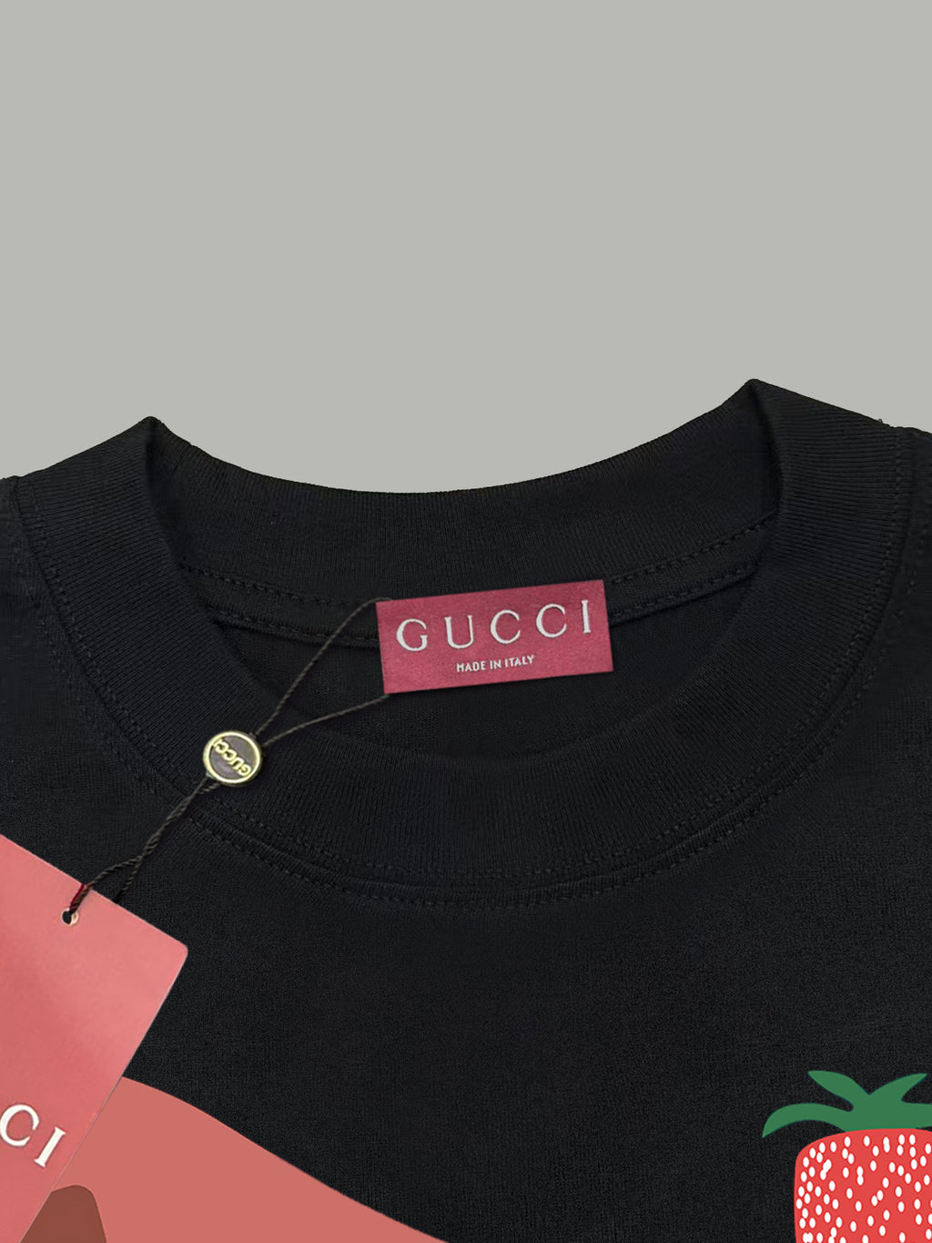 Black Gucci T-shirt collar with pink “GUCCI” label and strawberry chest graphic.