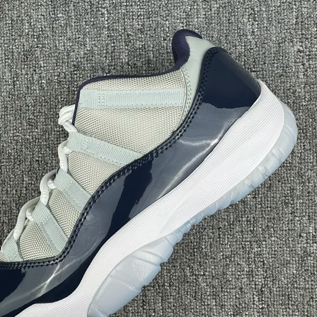 Close-up of low-top Jordan 11 sneaker side, cream mesh and navy glossy panel