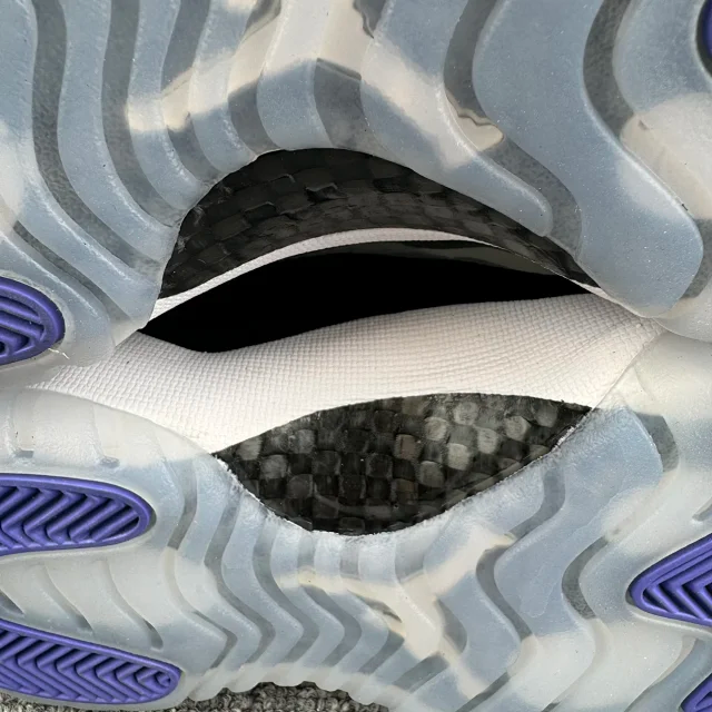 Low-top sneaker outsole close-up with blue tread pads and traction opening