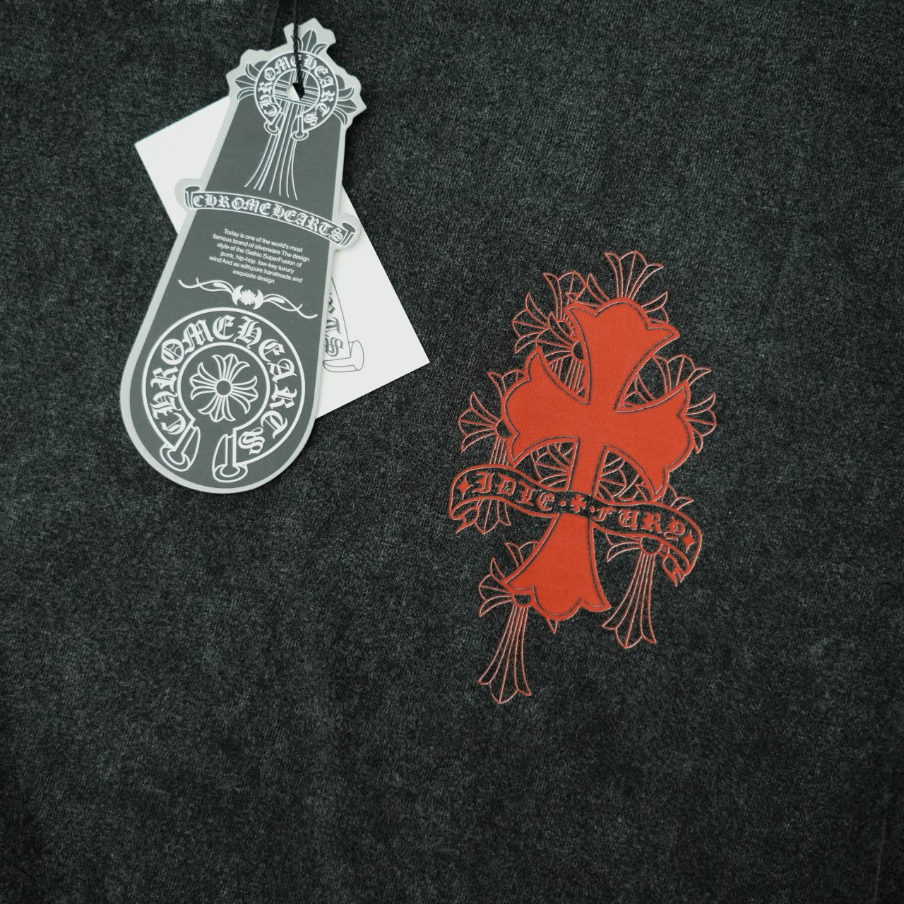 Dark T-shirt with orange-red cross-style graphic and white hang tag