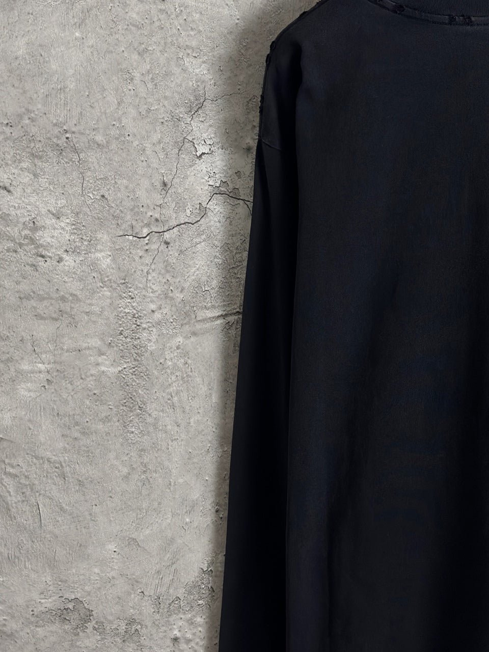 Black long-sleeve T-shirt back side view, plain fabric with minimal seam lines