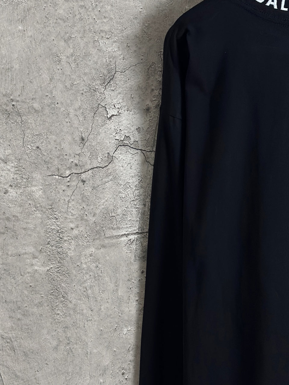 Balenciaga long-sleeve top side view, dark fabric with partial logo at top