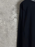 Balenciaga long-sleeve top side view, dark fabric with partial logo at top