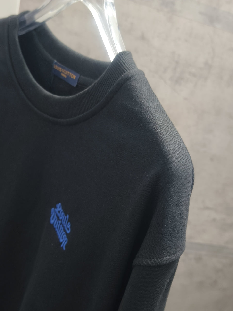 Dark long-sleeve crewneck sweatshirt with small blue logo on the sleeve