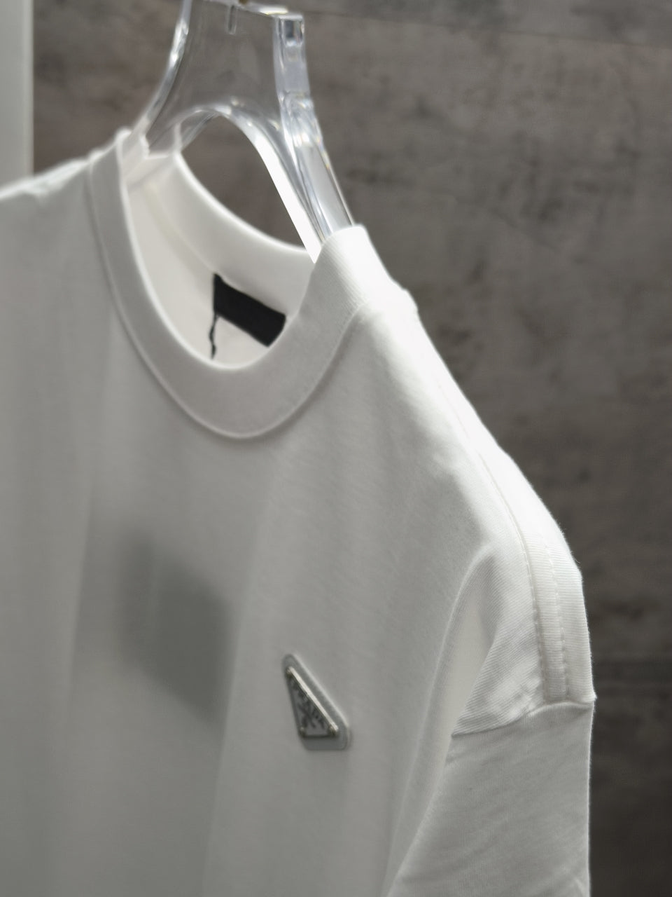 White short-sleeve T-shirt on clear hanger with triangular chest logo