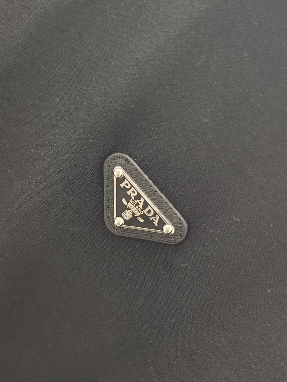 Triangular Prada logo patch on dark fabric