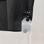 Black suit jacket sleeve cuff with three buttons and attached white tag pocket