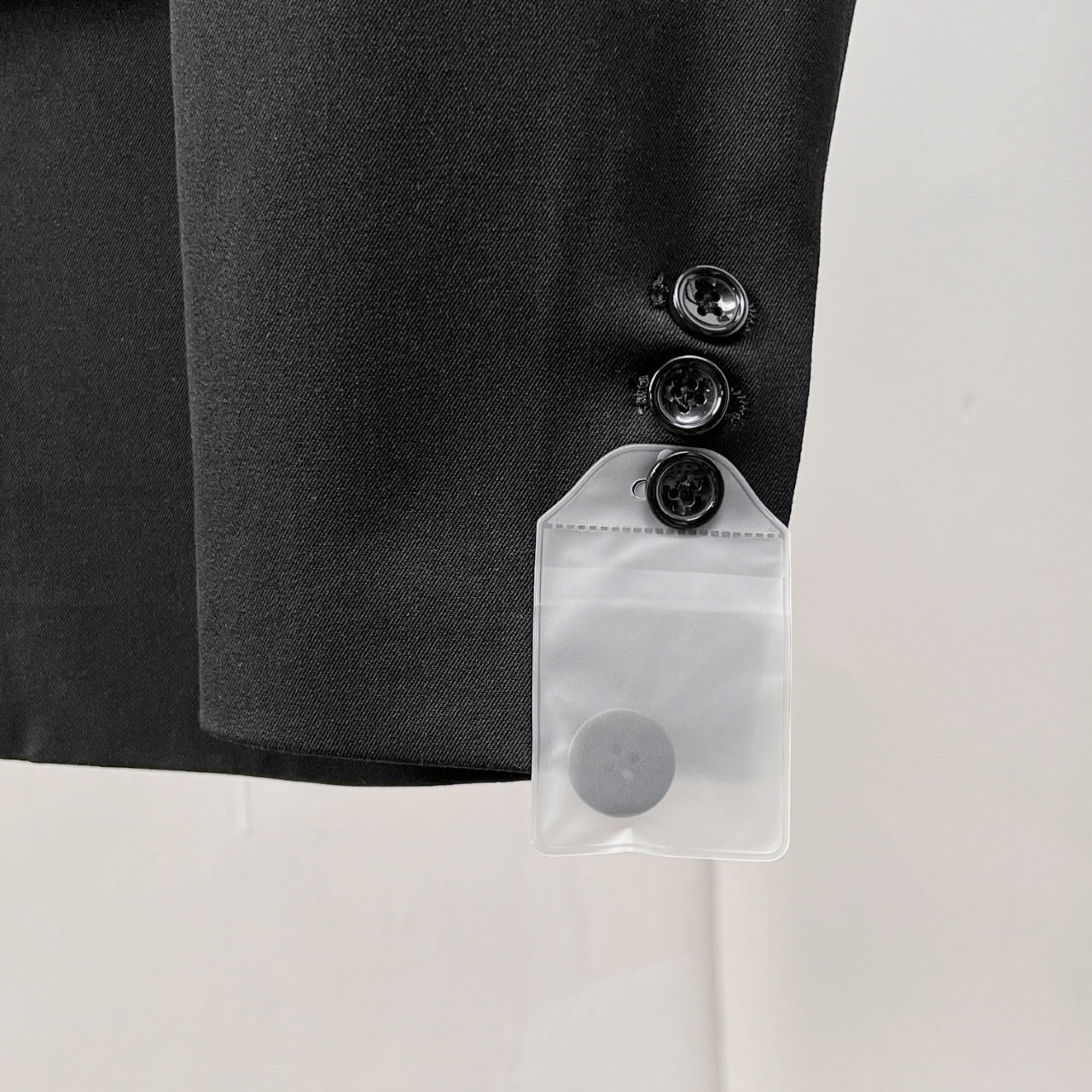 Black suit jacket sleeve cuff with three buttons and attached white tag pocket