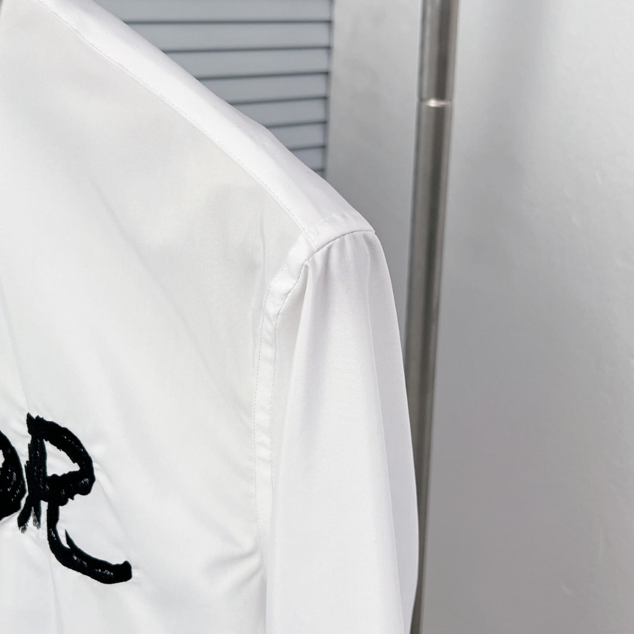 White button-up dress shirt shoulder seam with partial black graphic logo