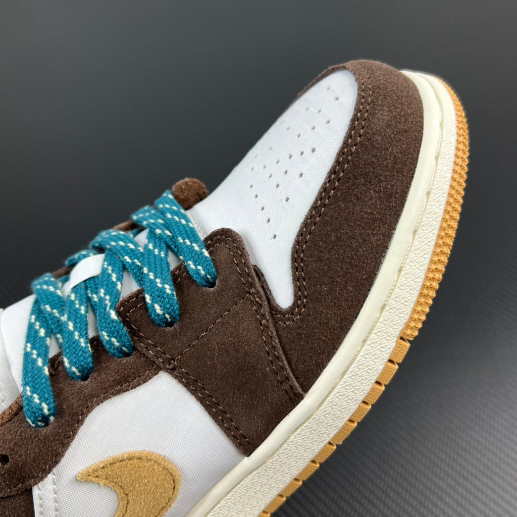 Low-top sneaker close-up with brown suede, white toe, teal laces, gold trim.