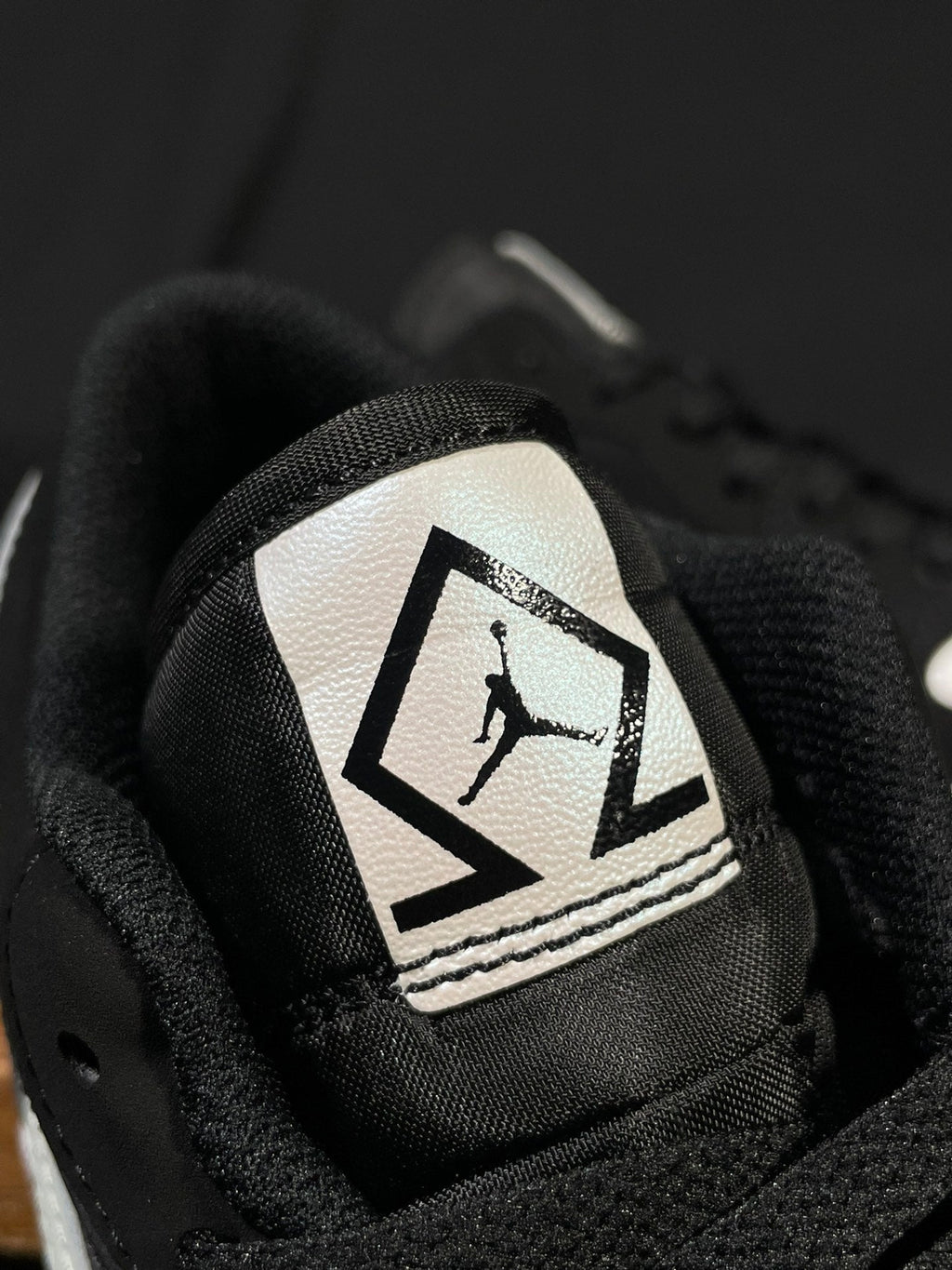 Black sneaker tongue patch with Jumpman-style graphic in a white label