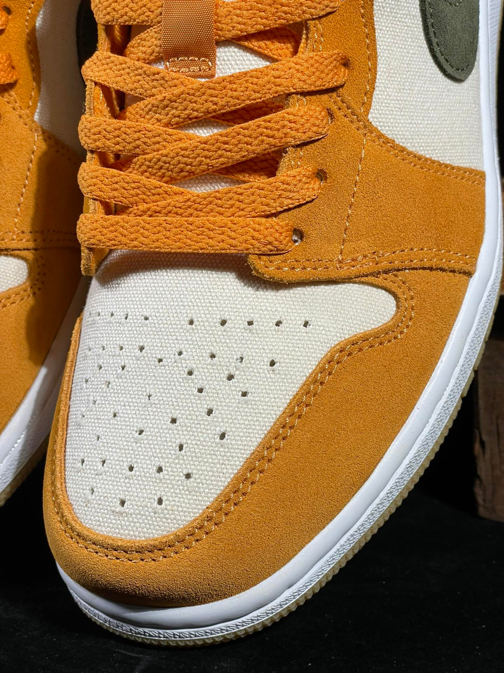 Close-up of orange laces and white perforated toe on orange and white low-top sneakers.