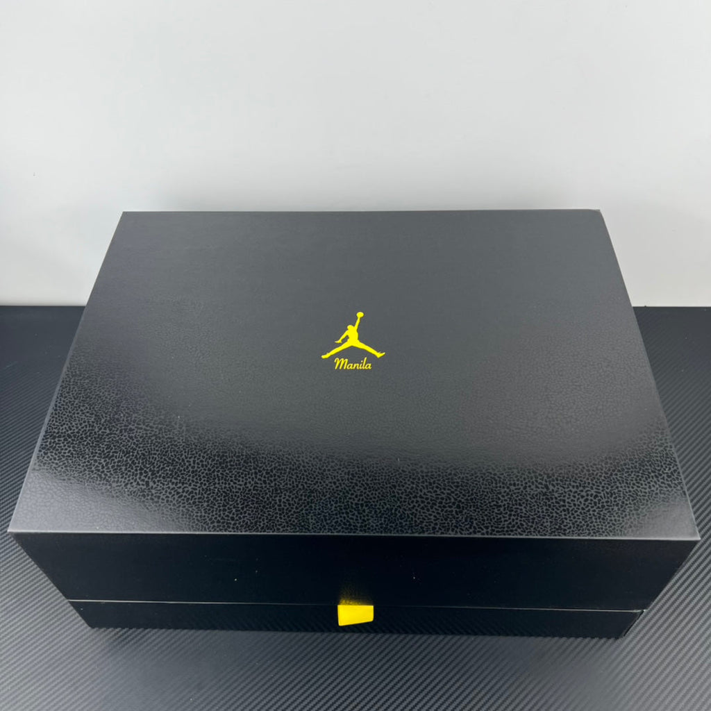 Dark shoe box lid with neon Manila Jumpman logo and yellow accent label