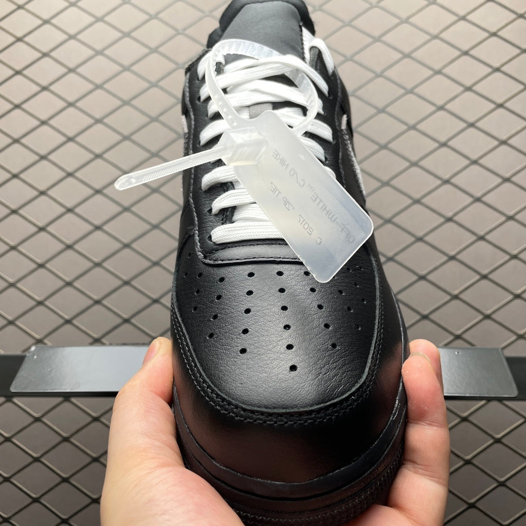 Black low-top sneaker with white laces, perforated toe, and rubber sole