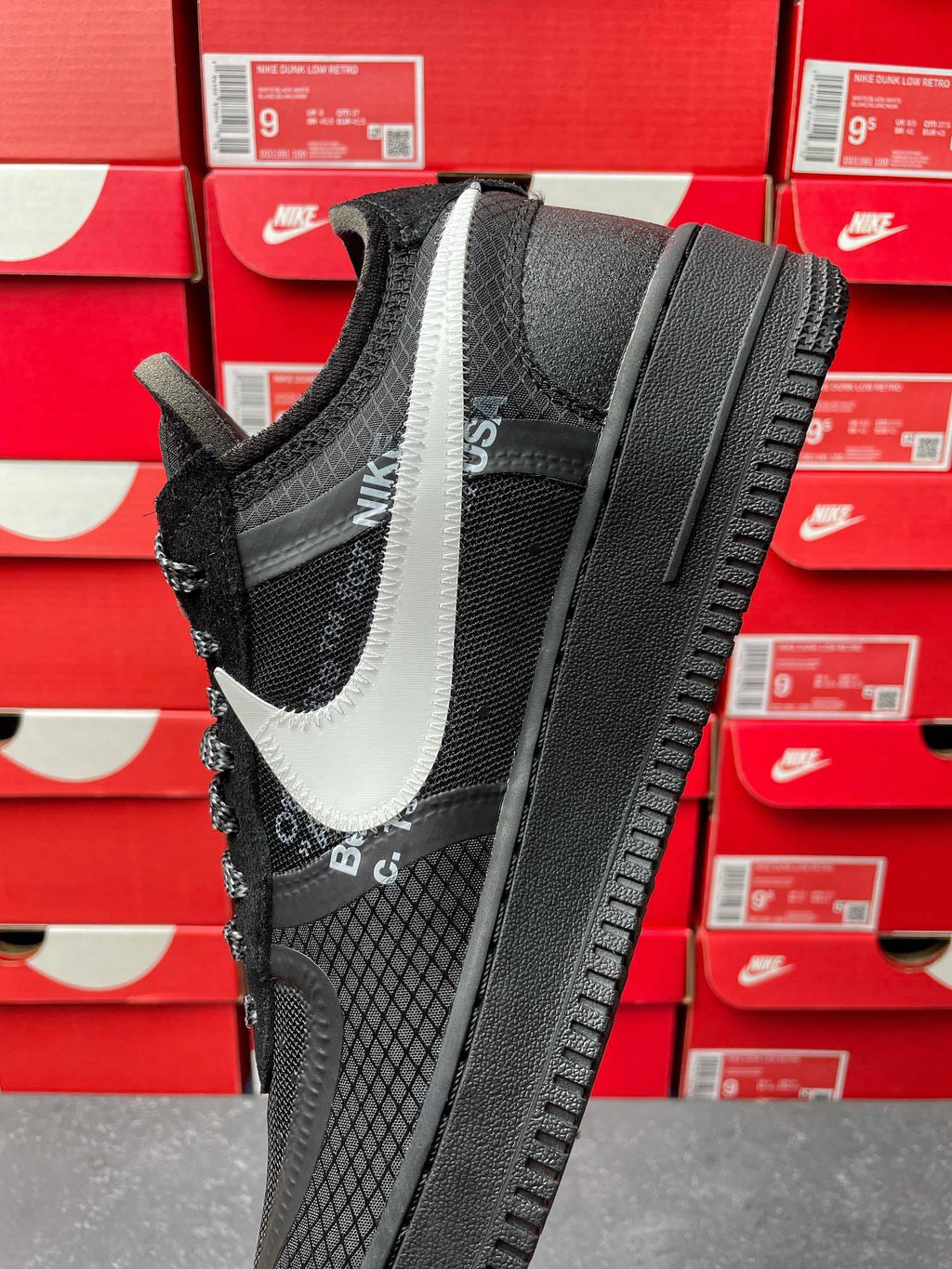 Black low-top sneaker with white swoosh, mesh sides, black laces, angled side view
