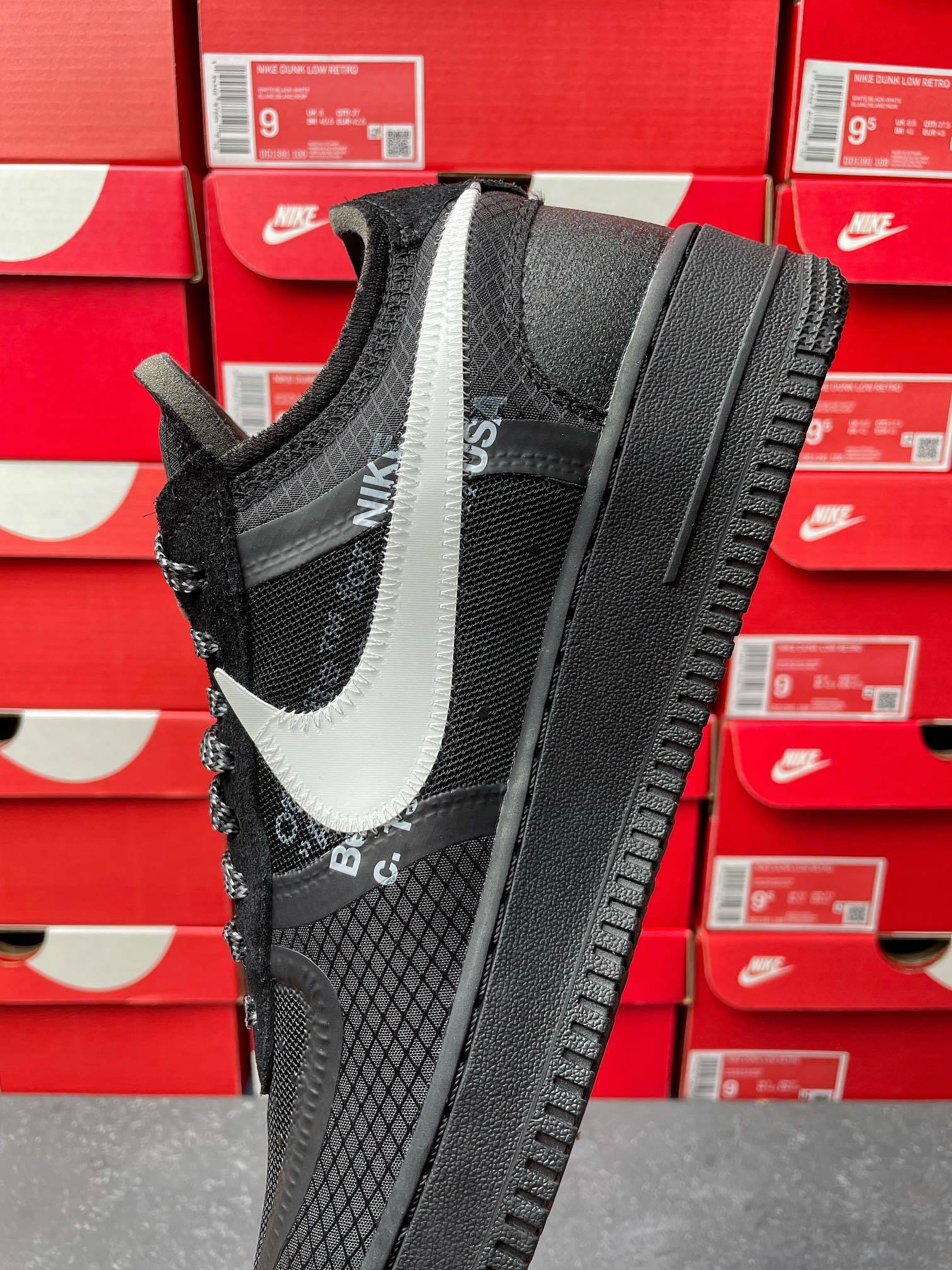 Black low-top sneaker with white swoosh, mesh sides, black laces, angled side view