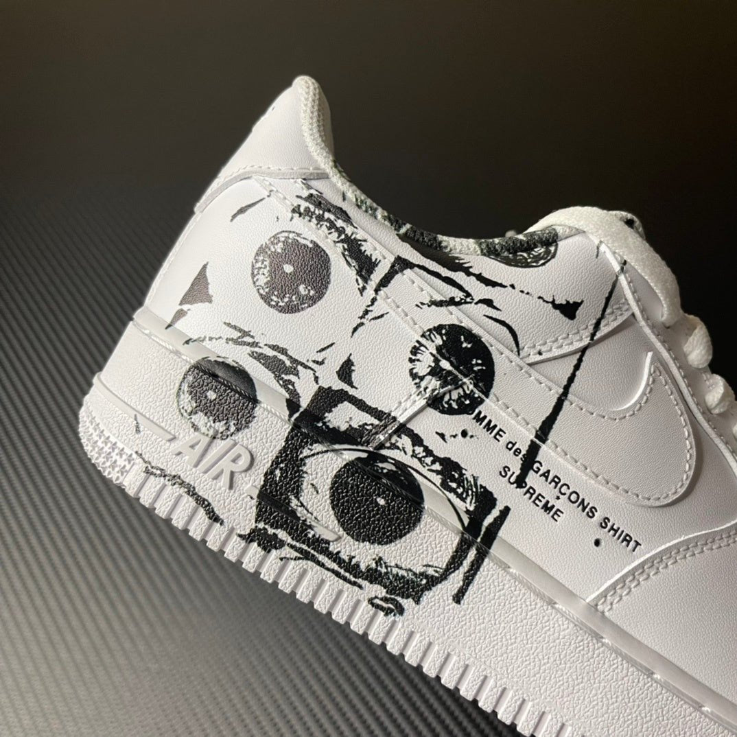 White low-top sneaker with black graphic wrap around laces and swoosh