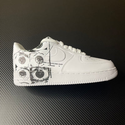 White low-top sneaker with black graphic panel on side and perforated toe