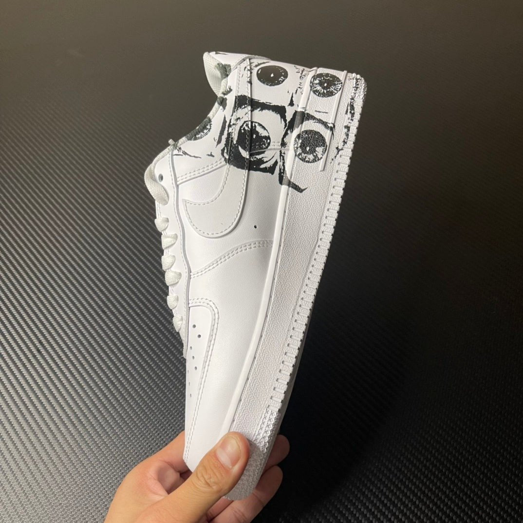White low-top sneaker held by hand, showing black graphic print near toe