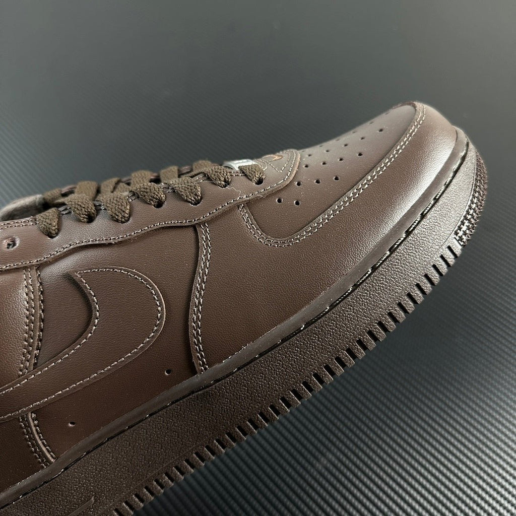 Taupe low-top sneaker side close-up with swoosh and lace eyelets, perforated toe.