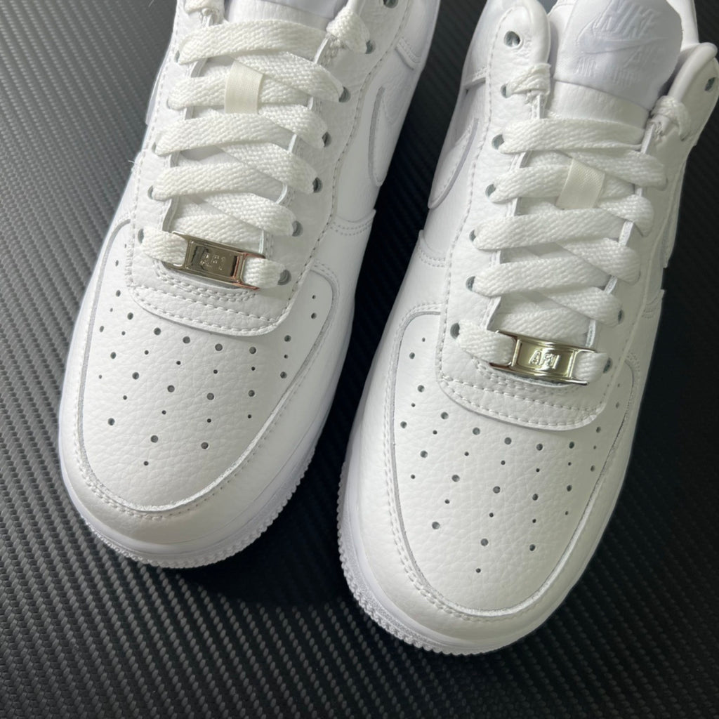 White sneakers front close-up with perforations and gold-toned buckle straps