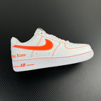 White low-top sneaker with orange Swoosh and side stitching, lace-up.