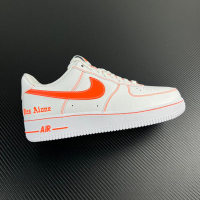 White low-top sneaker with orange Swoosh and side stitching, lace-up.