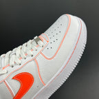 White low-top sneaker toe with orange laces and Swoosh detail.