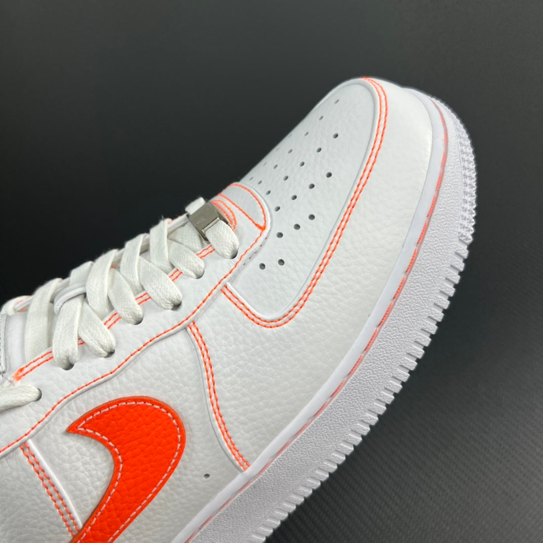 White low-top sneaker toe with orange laces and Swoosh detail.