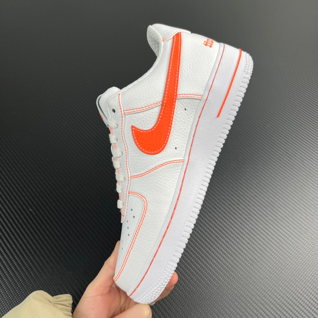 White low-top sneaker with orange Swoosh and stitched overlays, held in hand.