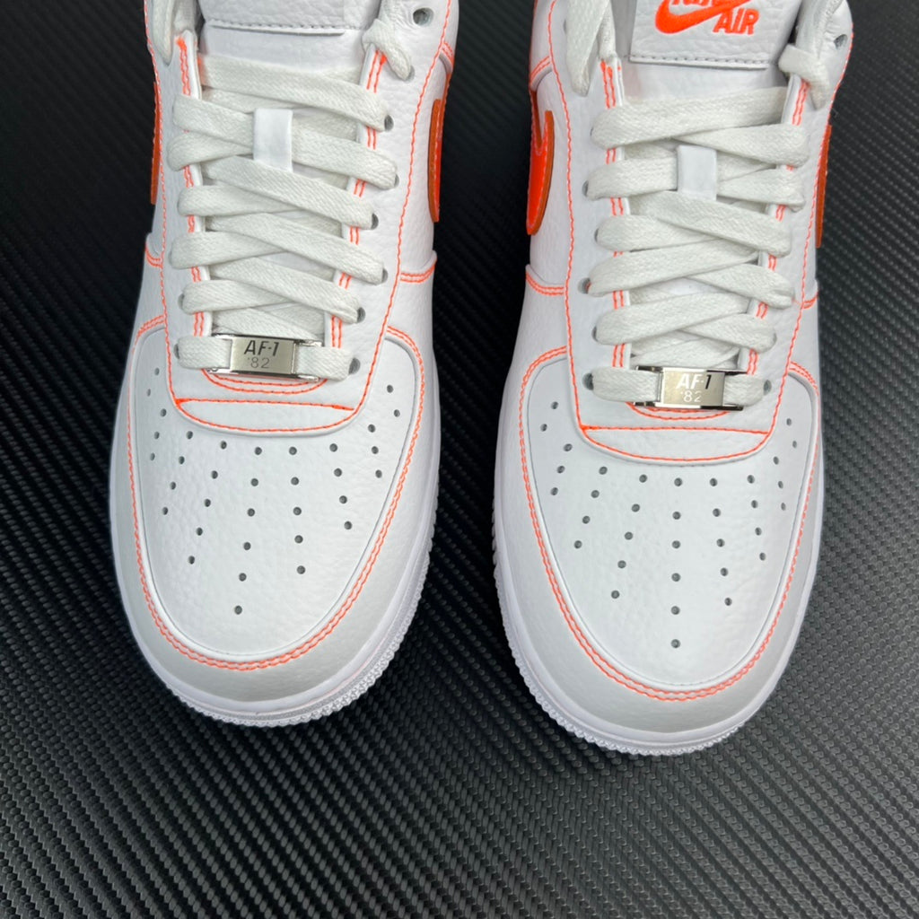Two white lace-up sneakers with orange piping and perforated toe panels.
