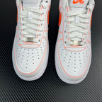 Two white lace-up sneakers with orange piping and perforated toe panels.