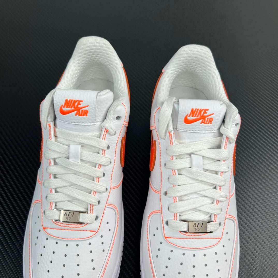 Two white sneakers with orange Swoosh on tongue and perforated toe panels.