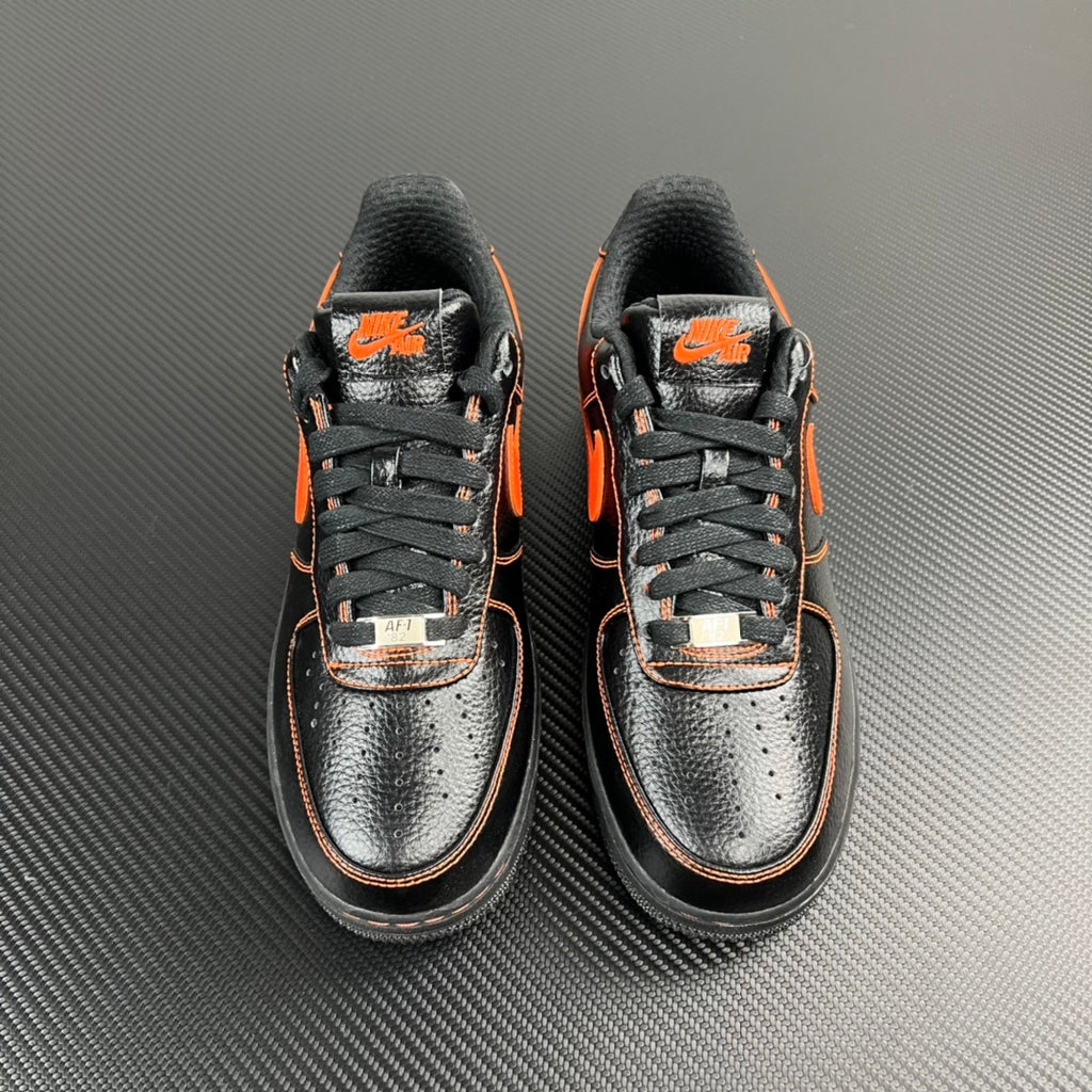 Pair of black and silver Air Force 1 sneakers with orange swooshes and laces