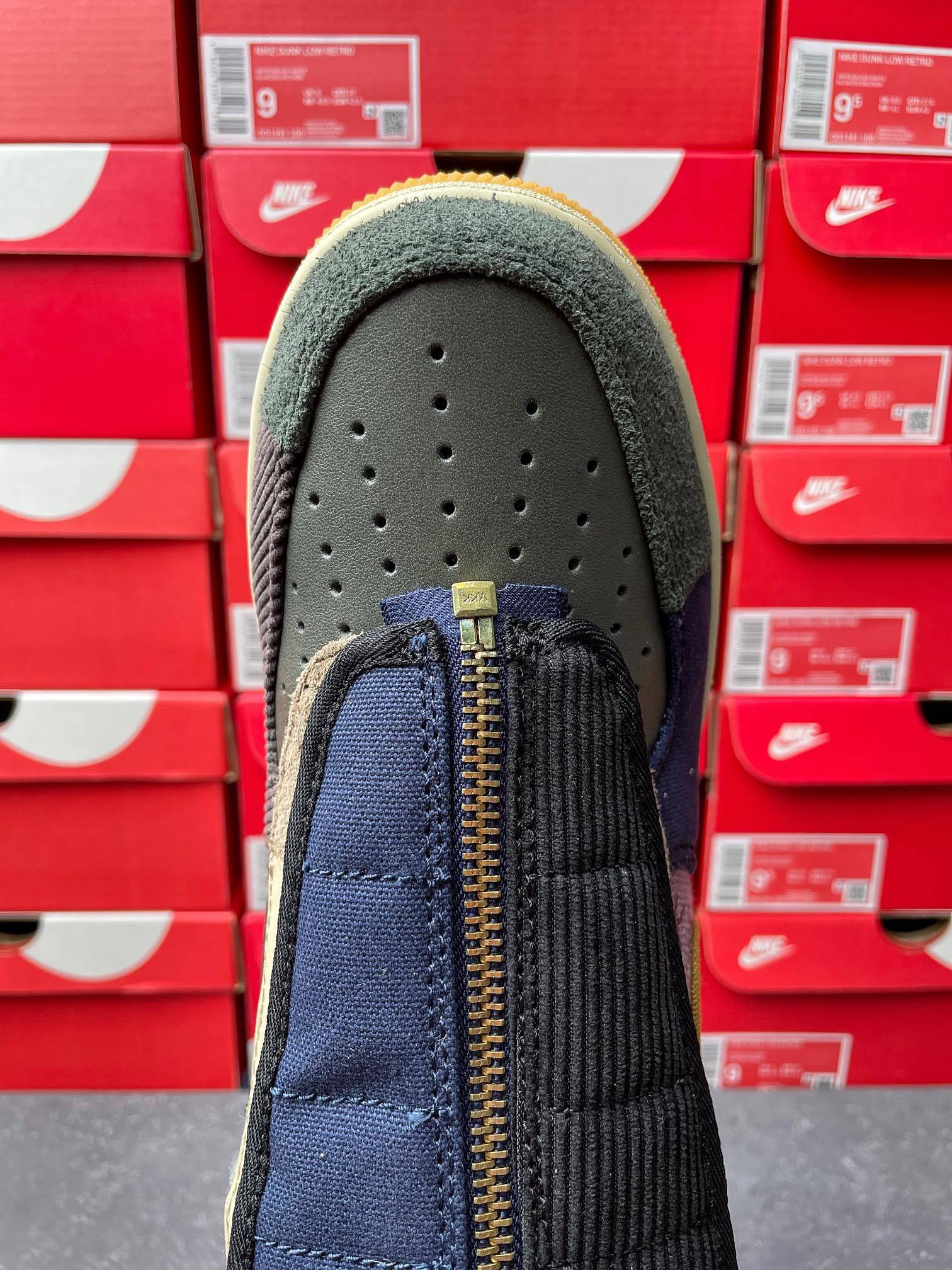 Low-top sneaker toe view with navy quarter panel, dark laces, and gold zipper detail