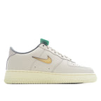 White Nike Air Force 1 sneakers with tan/gold swoosh and green lace loop