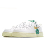 White leather low-top sneaker with gold swoosh, green accents, and tan gum outsole