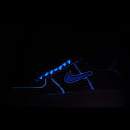 Dark-lit low-top sneaker with blue glowing swoosh and laces