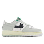 White sneaker with navy swoosh panel, green lace tab, perforated toe, and gum midsole.